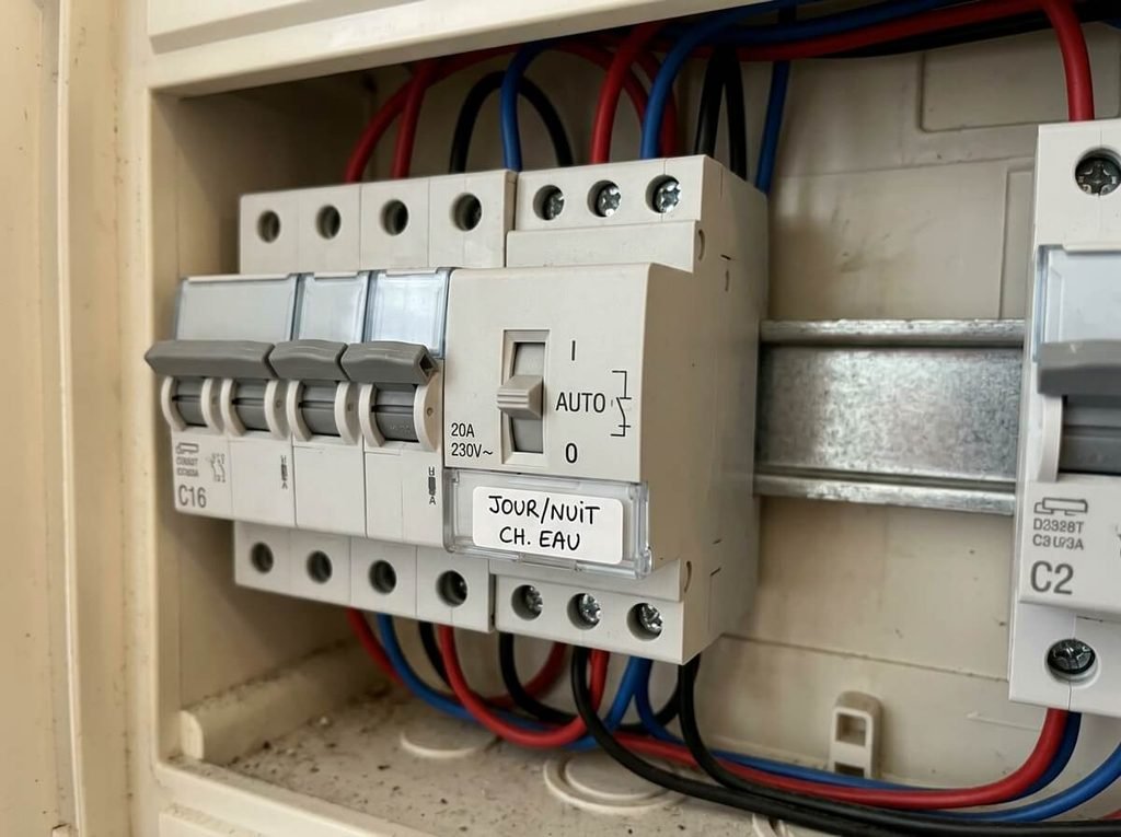 Module de contacteur jour nuit modulaire placé sur le rail DIN d'un tableau électrique domestique.